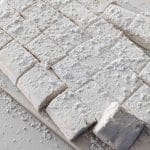vanilla bean marshmallows cut up on a white ceramic cutting board with powdered sugar around