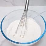 flour, baking powder and salt mixed together in a glass bowl with metal whisk