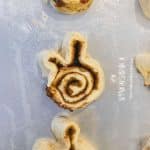 Slightly unroll each cinnamon roll by about 3 inches and shape the unrolled portion into an 'M' shape to make the bunny ears. Pinch the end of the ear into the side of the dough to help it stay together while baking for the cinnabunnies