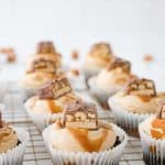 top snickers cupcakes with snickers, caramel sauce and peanuts