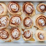 Heavy cream being poured over unbaked cinnamon rolls