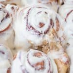 tangzhong cinnamon rolls in pan with Cream cheese frosting spread over warm cinnamon rolls