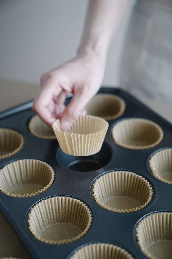 Hand placing brown cupcake liner in muffin baking tray, ready for baking.