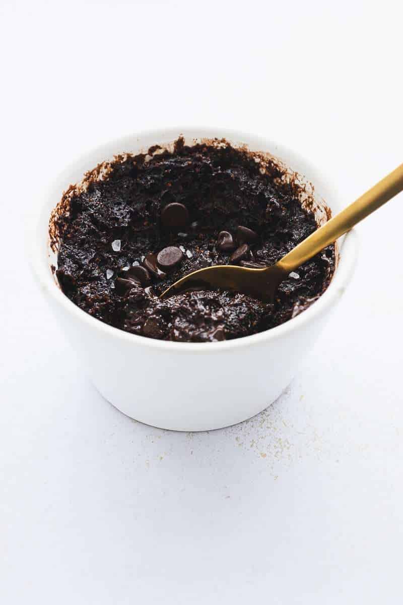 protein mug brownie cake in white ramekin with gold spoon taking a scoop