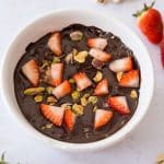 Dubai Chocolate Protein Brownie Mug Cake close up in rameking with chopped strawberries and pistachios on top and scattered around dish