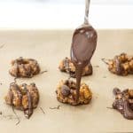 spoon drizzling chocolate over the tops of healthy samoa cookies on baking pan lined with natural parchment paper.