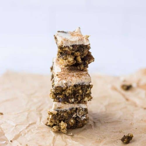 Cinnamon Rice Cake Protein Bars (with Dates & Cream Cheese Frosting) 3 stacked on top of each other on top of a piece of parchment paper