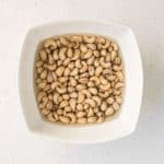 Raw cashews soaking in a white bowl of water