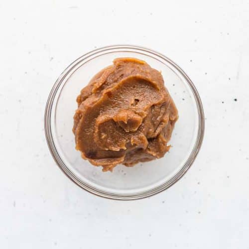 Blended dates and water mixed together to form date paste in a clear glass bowl on white surface