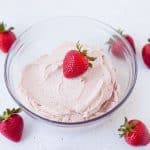 Strawberry vegan cashew buttercream frosting in clear glass bowl with strawberries around and one on top
