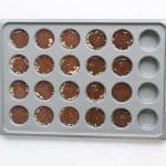 Sunbutter Oat Cups in mini muffin tins with melted chocolate on top & sprinkled sea salt on white background.