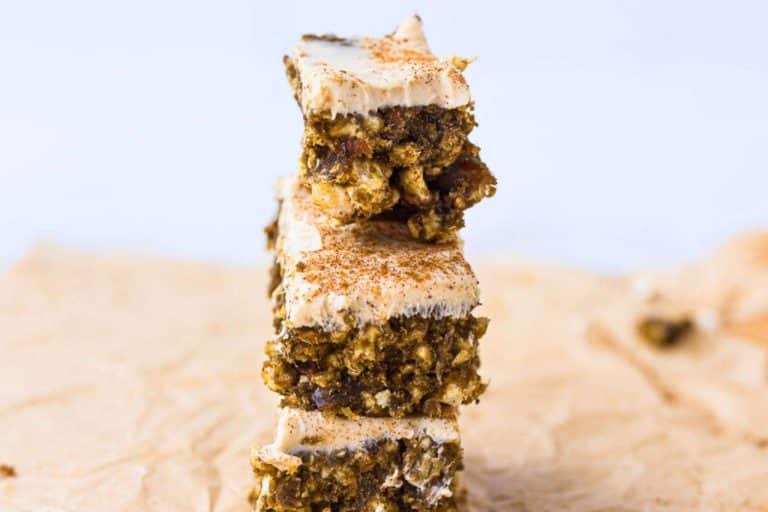 Cinnamon Rice Cake Protein Bars (with Dates & Cream Cheese Frosting) 3 stacked on top of each other on top of a piece of parchment paper