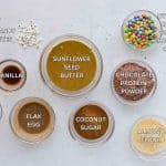 INGREDIENTS to make monster mash cookies in clear glass bowls on white surface