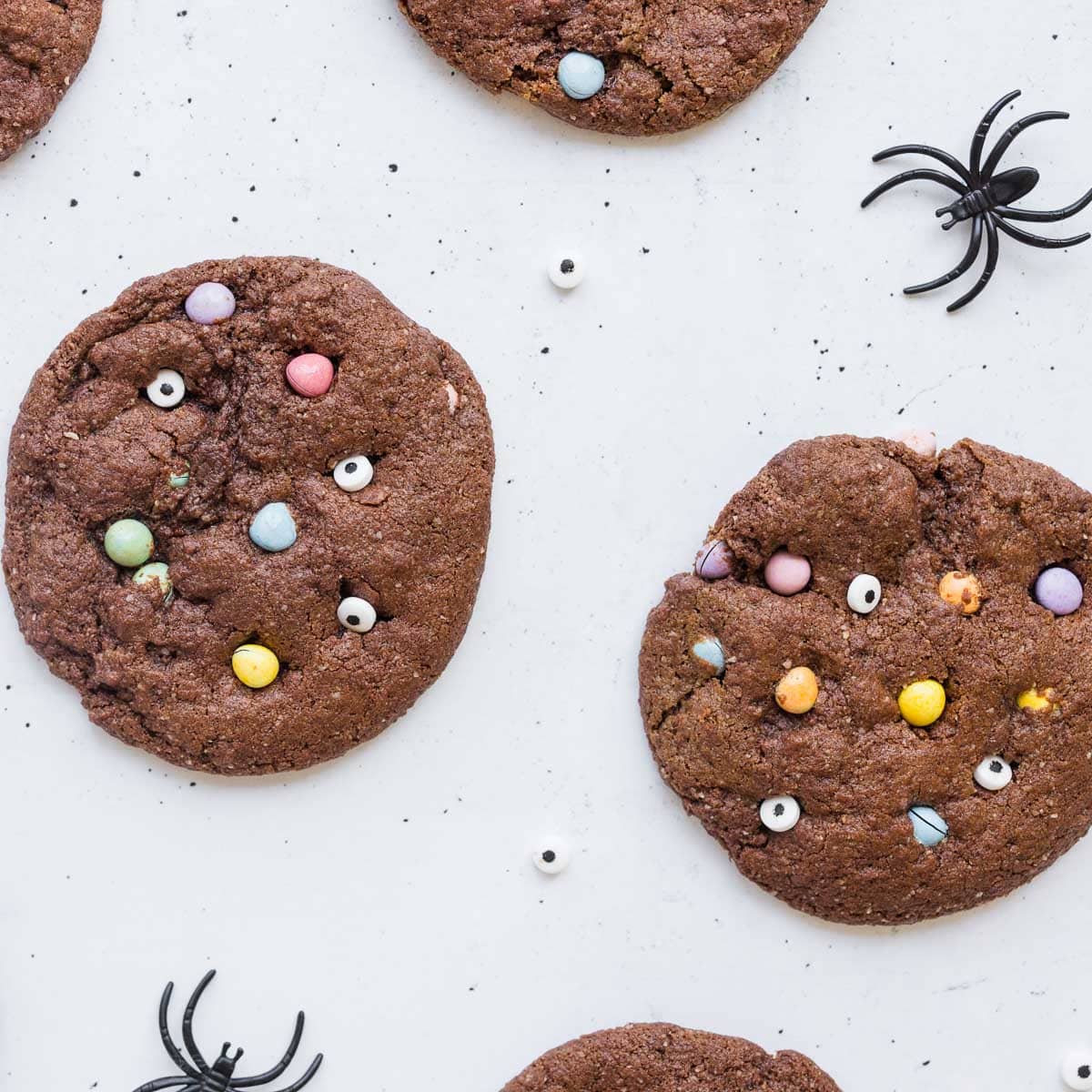 protein monster mash cookies on white surface with candy eyeballs and plastic spiders around