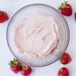 Vegan Strawberry Cashew Frosting in clear bowl with strawberries around on white surface