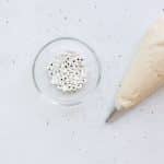 cashew frosting in a pumpkin tip fitted with a round tip and candy eyes in clear glass bowl on white surface