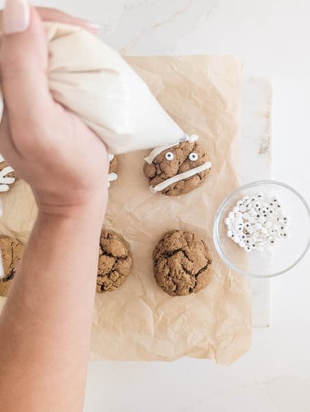 hand holding piping bag, piping mummy lines on vegan pumpkin spice cookie