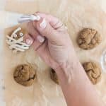 hand putting frosting on candy eye to put on vegan pumpkin spice cookie