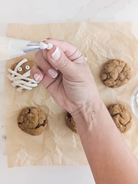 hand putting frosting on candy eye to put on vegan pumpkin spice cookie