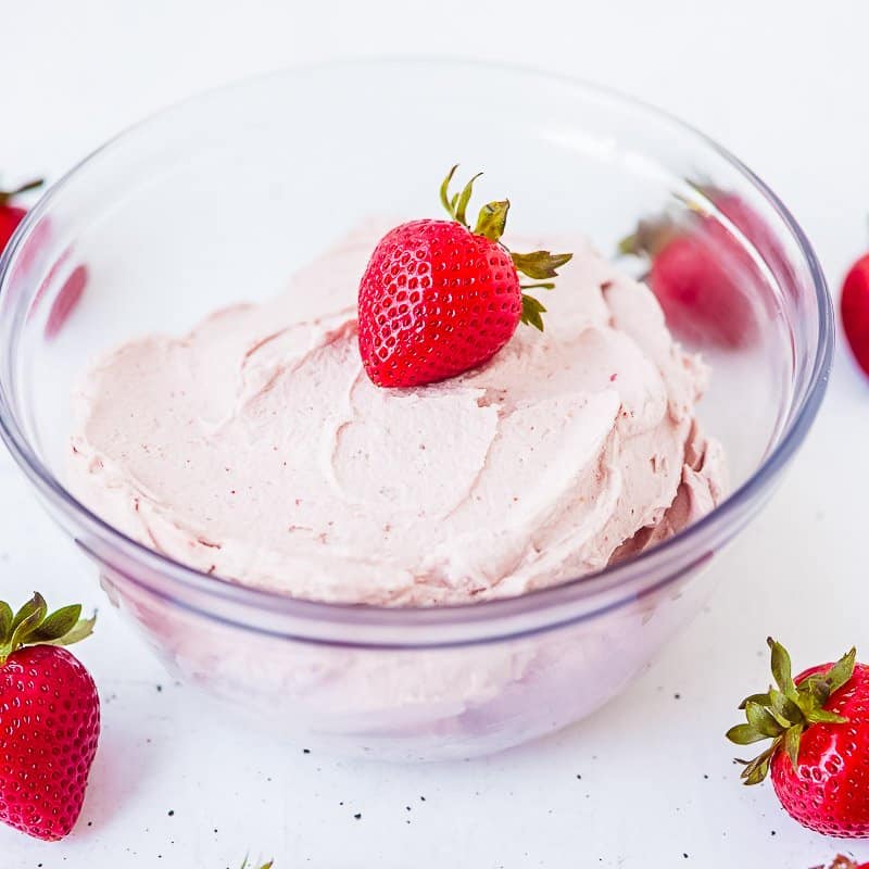 Strawberry vegan cashew buttercream frosting in clear glass bowl with strawberries around and one on top