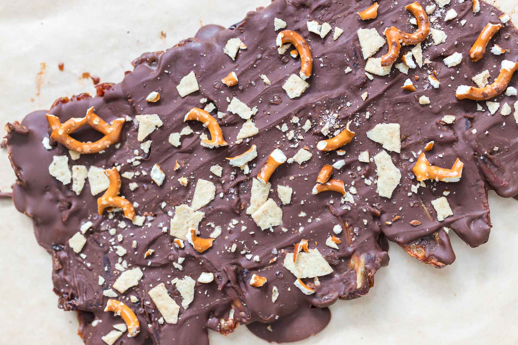 melted chocolate poured over the date layer, topped with pretzels and almond flour crackers for making christmas crack date bark.