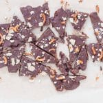 No-Bake Christmas Crack Date Bark broken into pieces on parchment paper, topped with chocolate, flaky sea salt, crushed gluten-free pretzels, and almond flour crackers. A festive, healthy, dairy-free, and gluten-free holiday dessert.