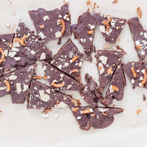 No-Bake Christmas Crack Date Bark broken into pieces on parchment paper, topped with chocolate, flaky sea salt, crushed gluten-free pretzels, and almond flour crackers. A festive, healthy, dairy-free, and gluten-free holiday dessert.