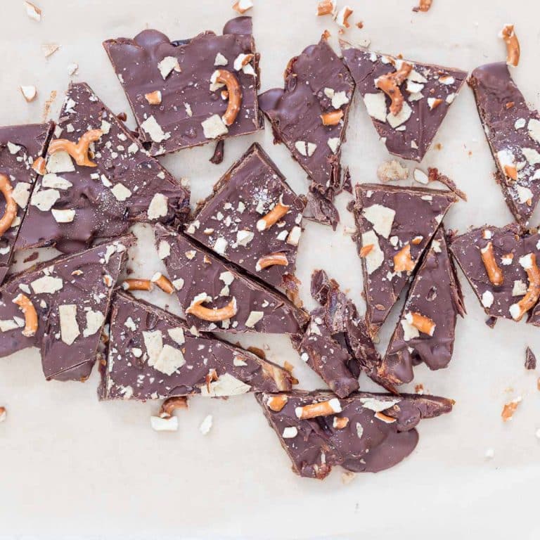 No-Bake Christmas Crack Date Bark broken into pieces on parchment paper, topped with chocolate, flaky sea salt, crushed gluten-free pretzels, and almond flour crackers. A festive, healthy, dairy-free, and gluten-free holiday dessert.