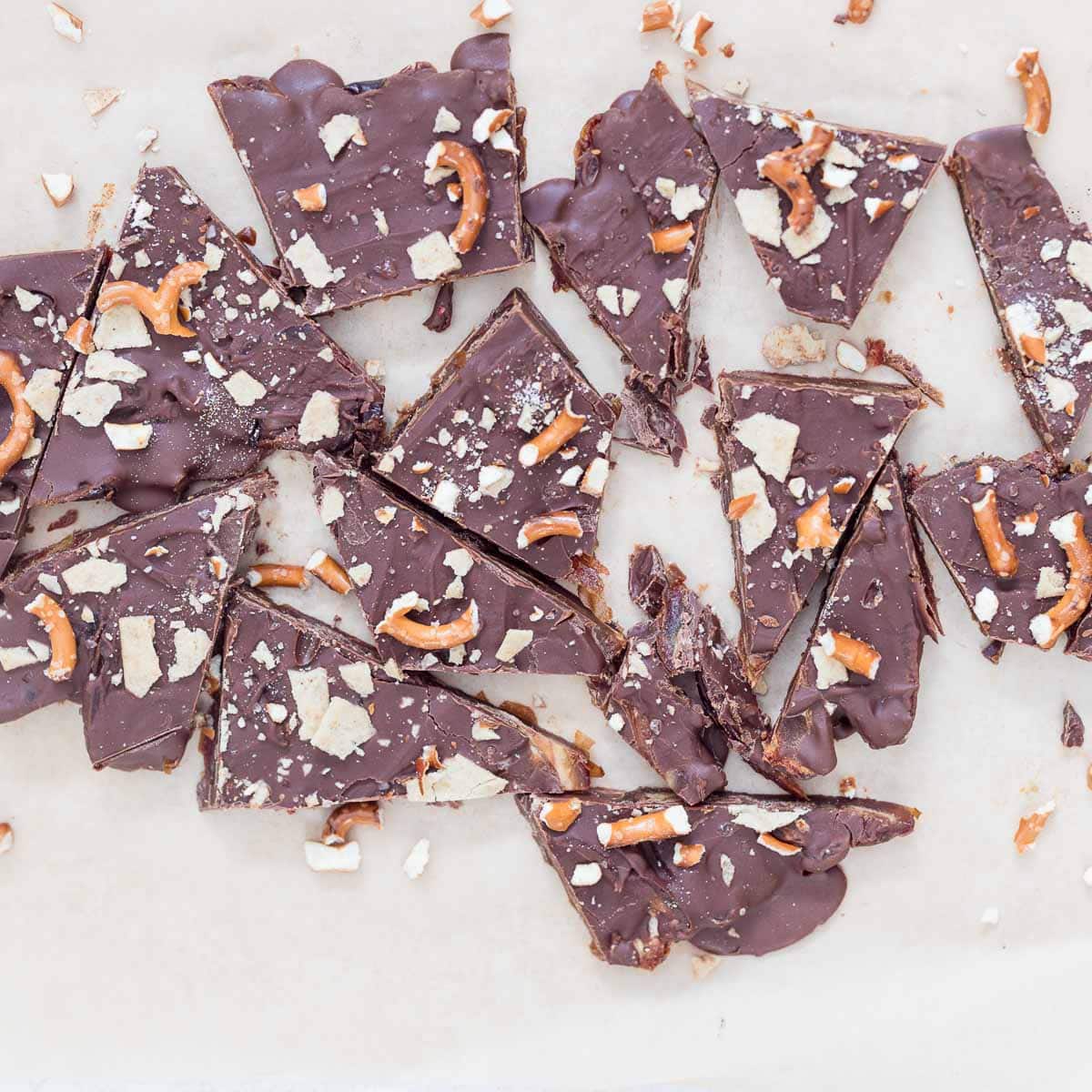 No-Bake Christmas Crack Date Bark broken into pieces on parchment paper, topped with chocolate, flaky sea salt, crushed gluten-free pretzels, and almond flour crackers. A festive, healthy, dairy-free, and gluten-free holiday dessert.