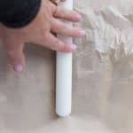 hand using rolling pin to flatten Medjool dates inbetween parchment paper to make Christmas Crack Date Bark