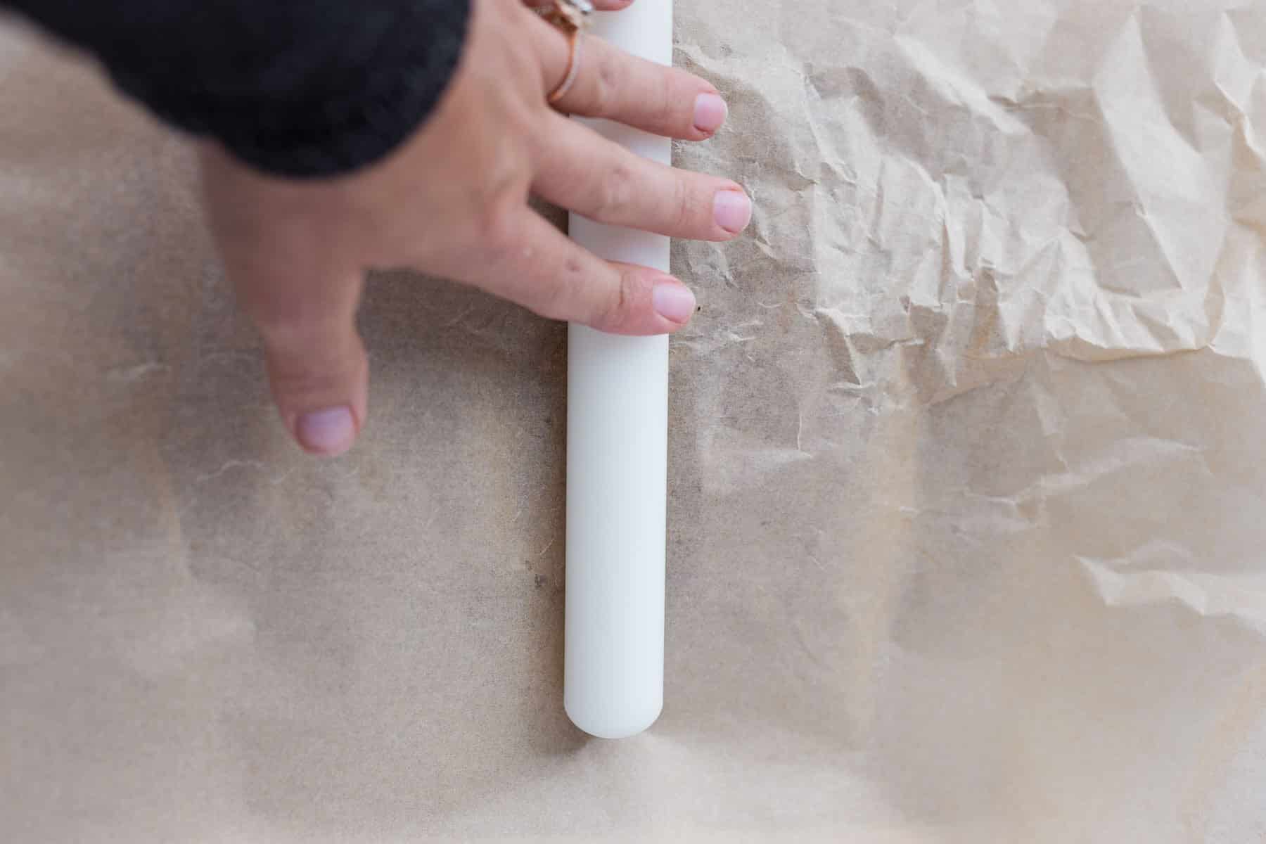 hand using rolling pin to flatten Medjool dates inbetween parchment paper to make Christmas Crack Date Bark