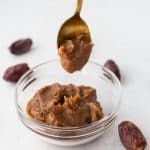 date paste in clear glass bowl with gold spoon above holding scoop of the paste