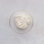 protein cream cheese greek yogurt frosting in clear glass bowl on white speckled surface