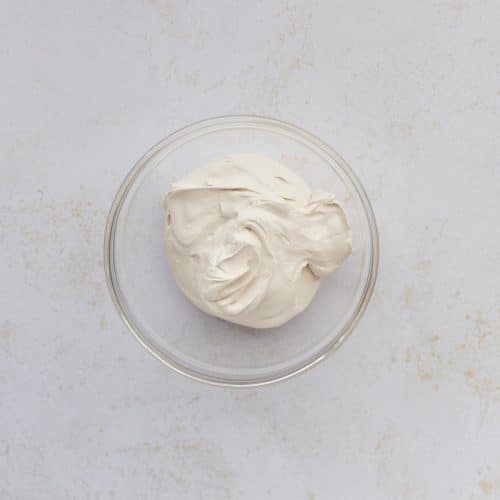 protein cream cheese greek yogurt frosting in clear glass bowl on white speckled surface