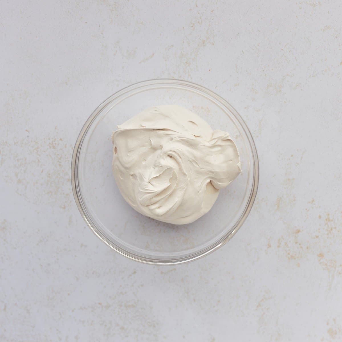 protein cream cheese greek yogurt frosting in clear glass bowl on white speckled surface