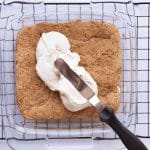 Spreading creamy protein frosting evenly over cooled sugar cookie protein bars.