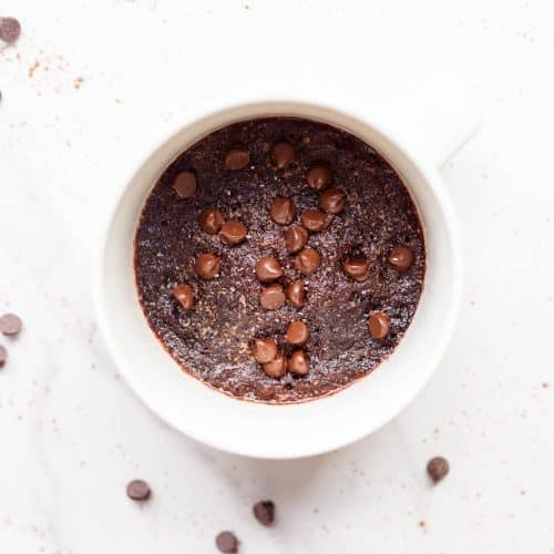 Pumpkin Spice Protein Mug Cake in white mug on white surface with chocolate chips around