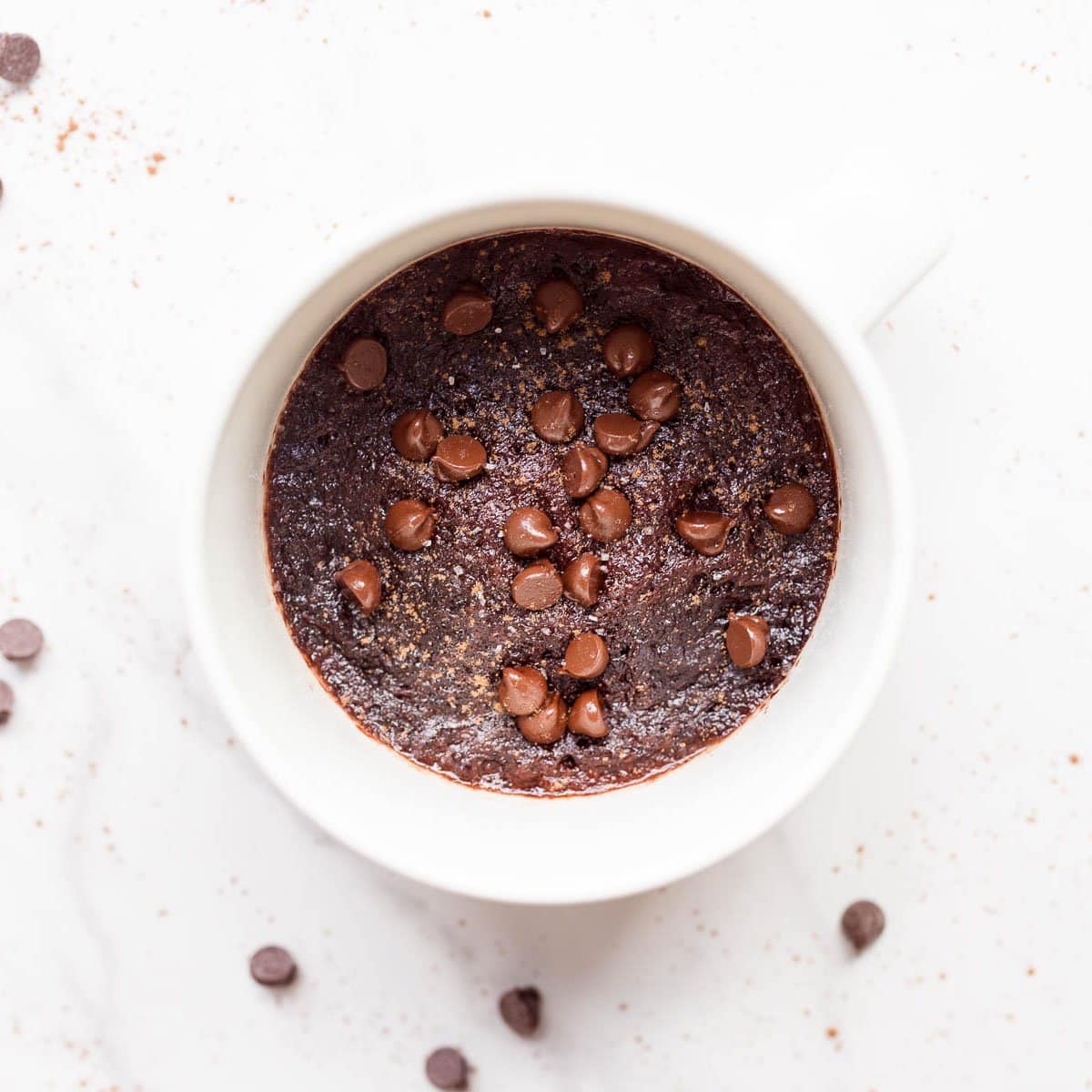 Pumpkin Spice Protein Mug Cake in white mug on white surface with chocolate chips around
