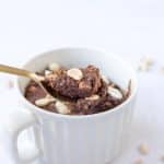 Soft and fudgy chocolate peanut butter protein mug cake with a bite taken out on a gold spoon