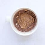 Ingredients for healthy Snickers protein mug cake mixed with maple syrup caramel drizzle.