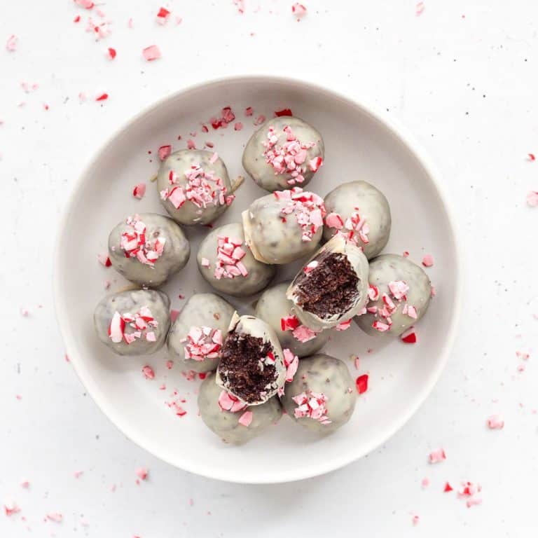 No-bake peppermint protein balls arranged on parchment paper, coated in white chocolate, and sprinkled with peppermint bits.