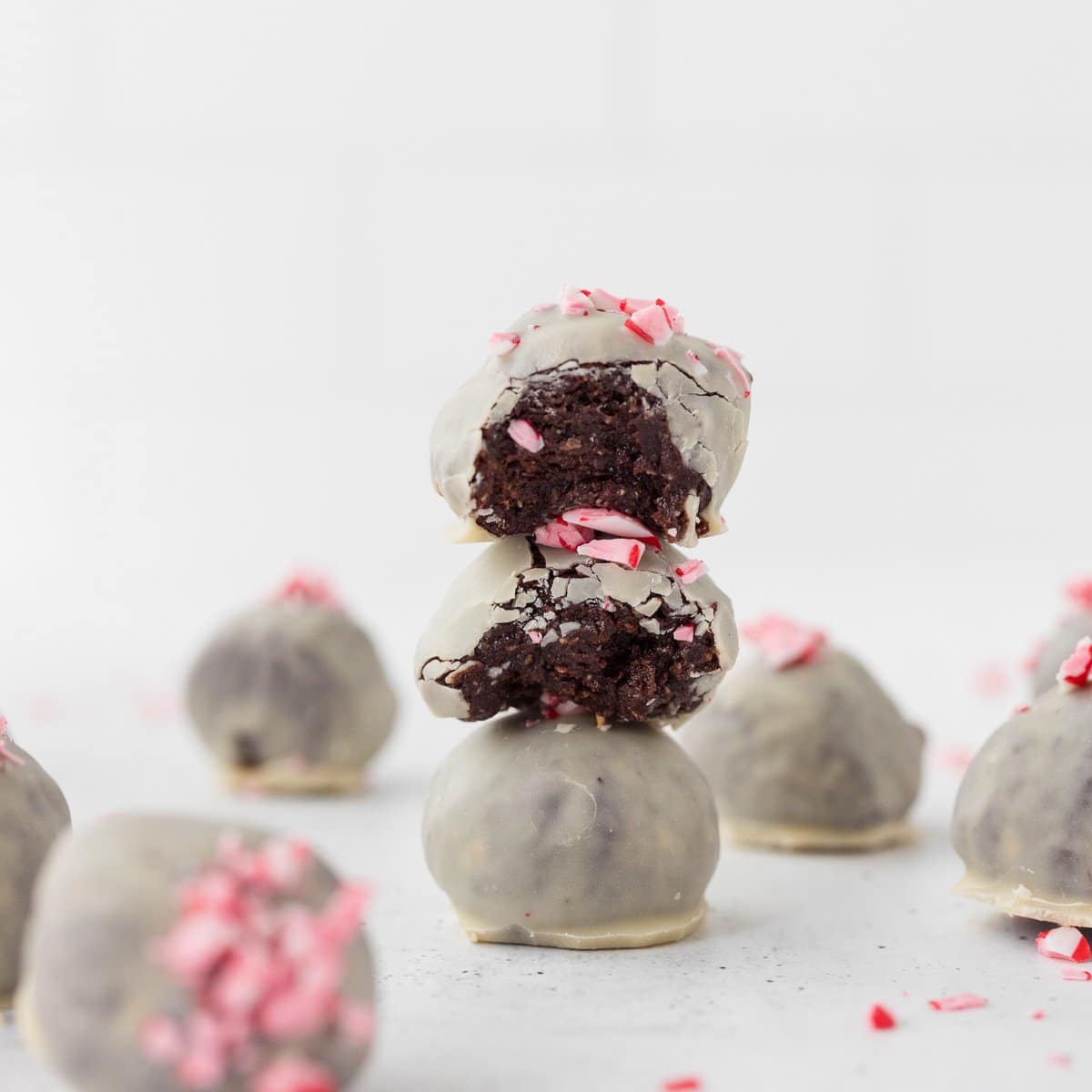 Close-up of 3 peppermint chocolate protein balls coated in white chocolate and sprinkled with crushed peppermint candies stacked on top of each other with bites taken out of the top 2.