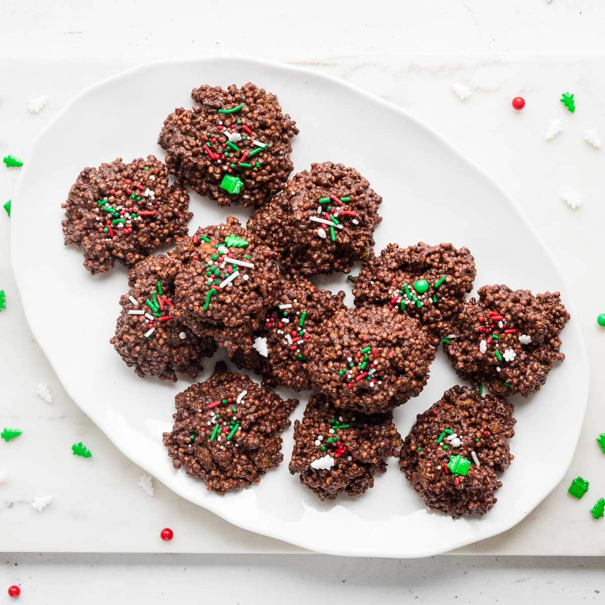 Overhead view of no-bake Biscoff chocolate quinoa clusters arranged on white scalloped plate with sprinkles around