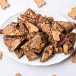 Sliced gingerbread date bark with chocolate and cookie crunch on white scalloped plate with gingerbread men around
