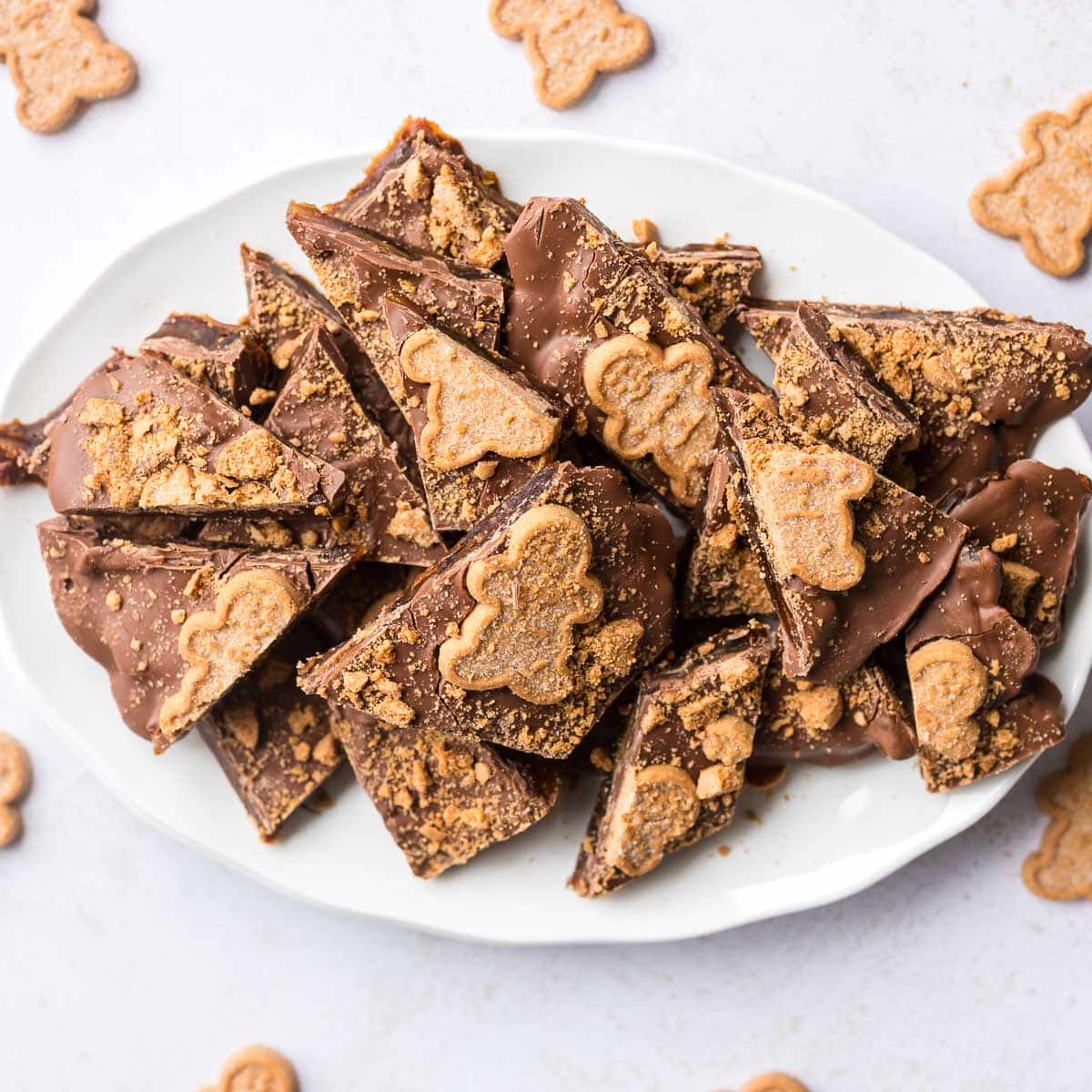 Sliced gingerbread date bark with chocolate and cookie crunch on white scalloped plate with gingerbread men around