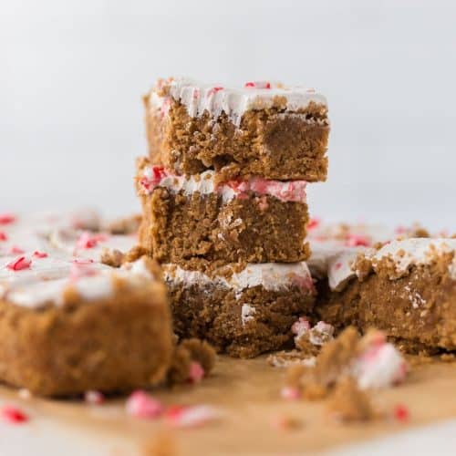 3 peppermint sugar cookie bars stacked on top of each other with bite taken out and others around on natural parchment paper