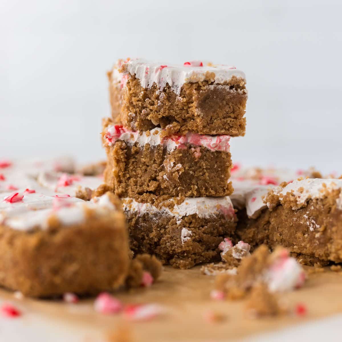 3 peppermint sugar cookie bars stacked on top of each other with bite taken out and others around on natural parchment paper