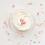 peppermint protein frosting in clear glass bowl with crushed peppermint candies around