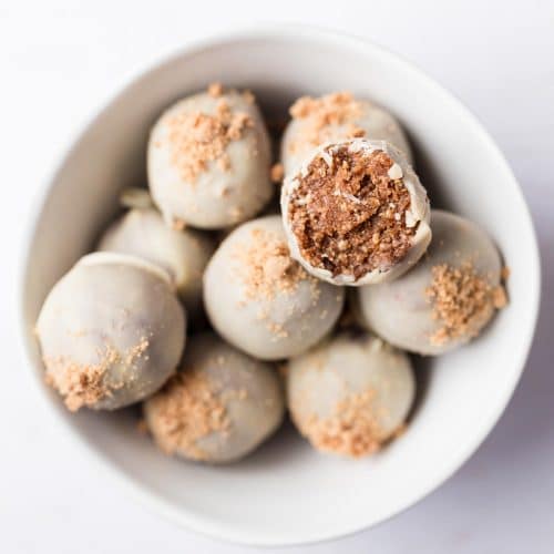 Healthy gingerbread energy bites coated in white chocolate in a white bowl on a white surface
