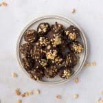 Snickers protein balls on a white plate, made with dates, peanut butter, chocolate, and topped with chopped peanuts